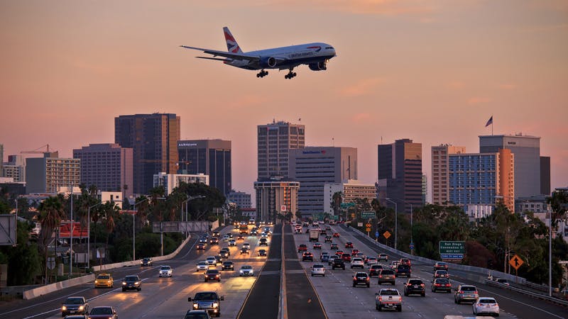 Jet aircraft on landing approach flying low over city freeway.