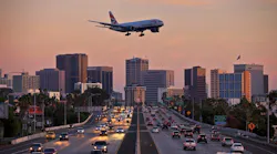 Jet aircraft on landing approach flying low over city freeway.