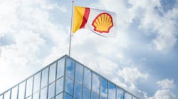 Shell flag flying on top of glass building against blue sky and cloud backdrop Shell flag flying on top of glass building against blue sky and cloud backdrop
