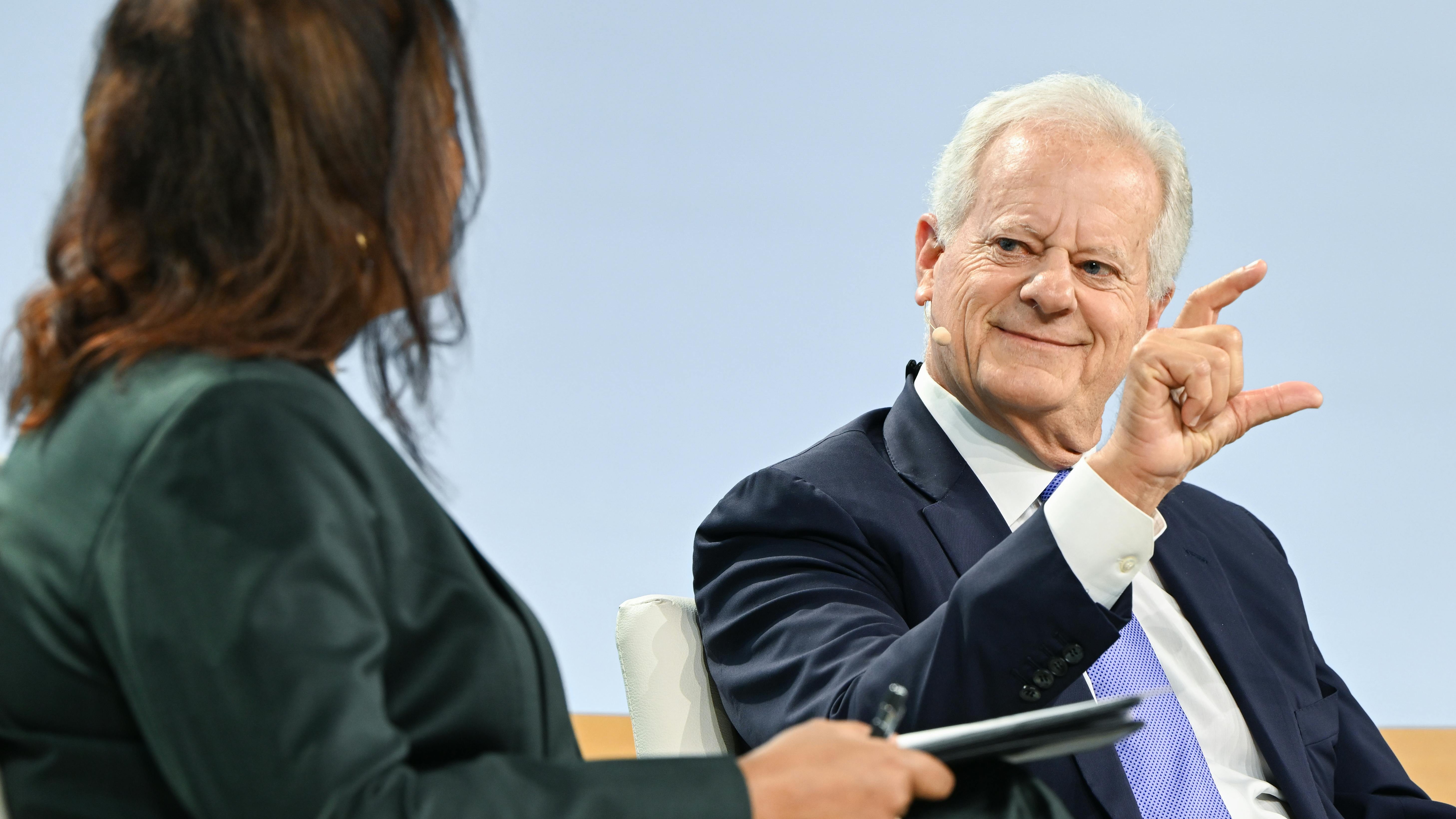 a woman and a man dressed in suits sit facing each other at a conference discussion