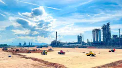 Construction vehicles undertaking site-preparation works in front of a refinery background.