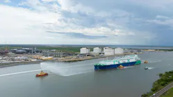 Tanker containing first shipment from the Golden Pass LNG project is guided by tug vessels through a canal waterway out to open sea.