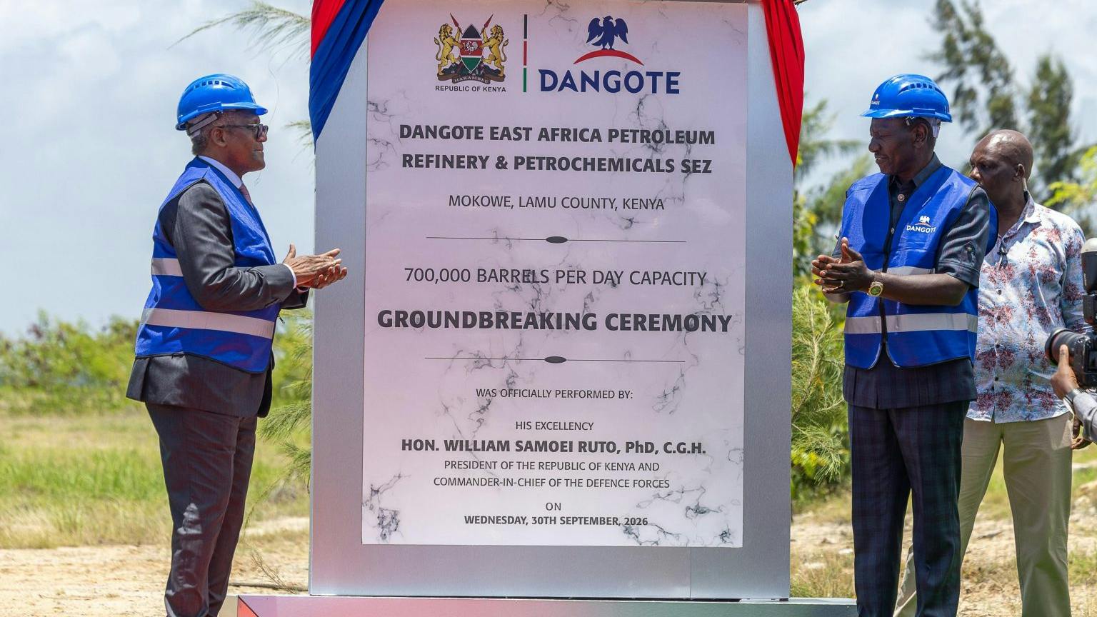Large sign with red and blue ribbons draped along sides announcing future site of the Lamu refinery.