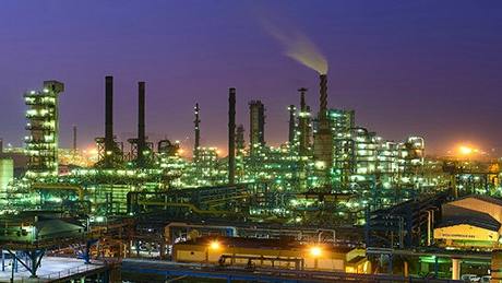 Panoramic view of illuminated processing and production installations at HPCL's Mumbai refinery at night against a purple-bluish sky.