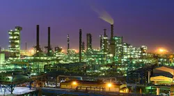 Panoramic view of illuminated processing and production installations at HPCL's Mumbai refinery at night against a purple-bluish sky.