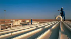 Workers stand on white storage tanks pointing to the blue-sky horizon at Melehia field in the western Egyptian desert.