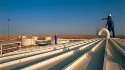 Workers stand on white storage tanks pointing to the blue-sky horizon at Melehia field in the western Egyptian desert.