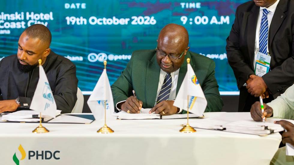 Signing ceremony for MOU to develop the second phase of PHDC's three-phased downstream petroleum showing two men at a table signing documents in front of blue-and-white banner background.